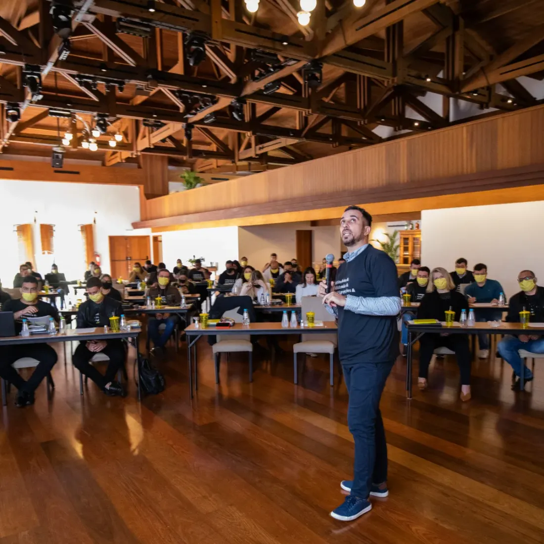 Bira conduzindo uma palestra em formato de conversa, com microfone, diante de uma plateia